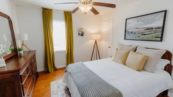 Une chambre à coucher comprenant un lit, une commode, un ventilateur de plafond, une lampe et un tableau accroché au mur.