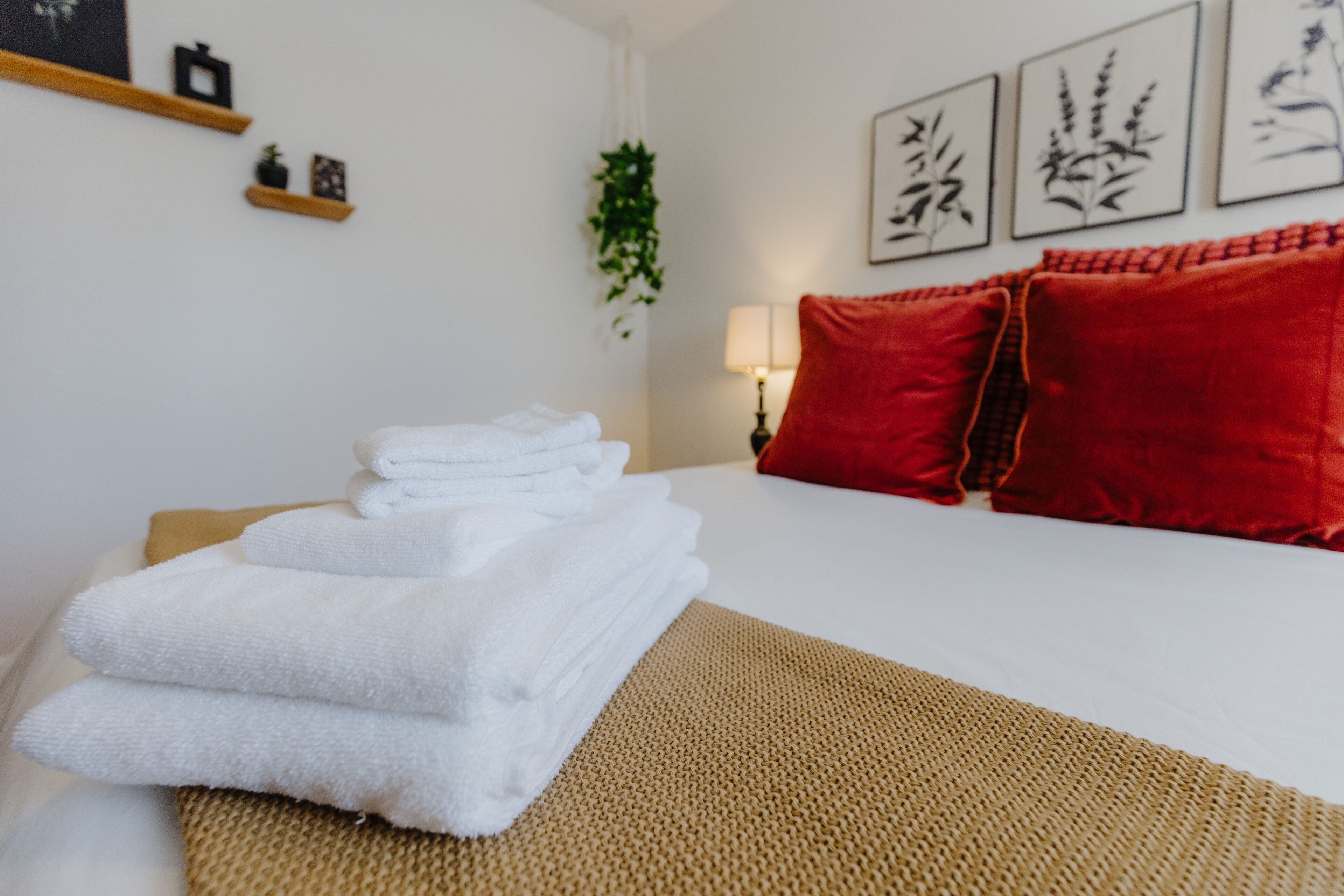 Un lit bien fait, avec des serviettes blanches, des coussins rouges et un tapis tissé.