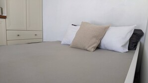 Un lit avec un matelas gris, des oreillers blancs et un plaid beige.