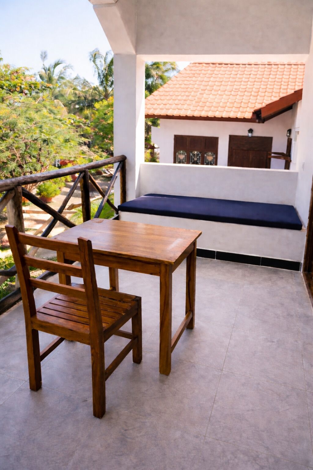 A wooden table and chair on a balcony with a view of a house and greenery.