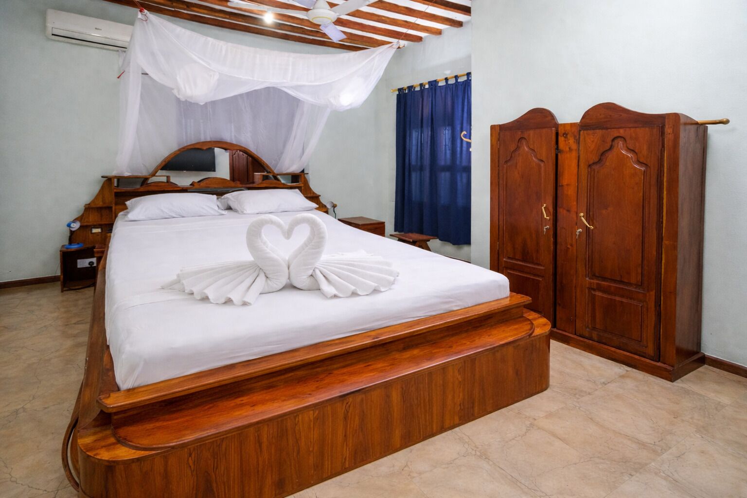 Een bed met een handdoek opstelling in de vorm van een hart, een houten garderobe en een plafondventilator.