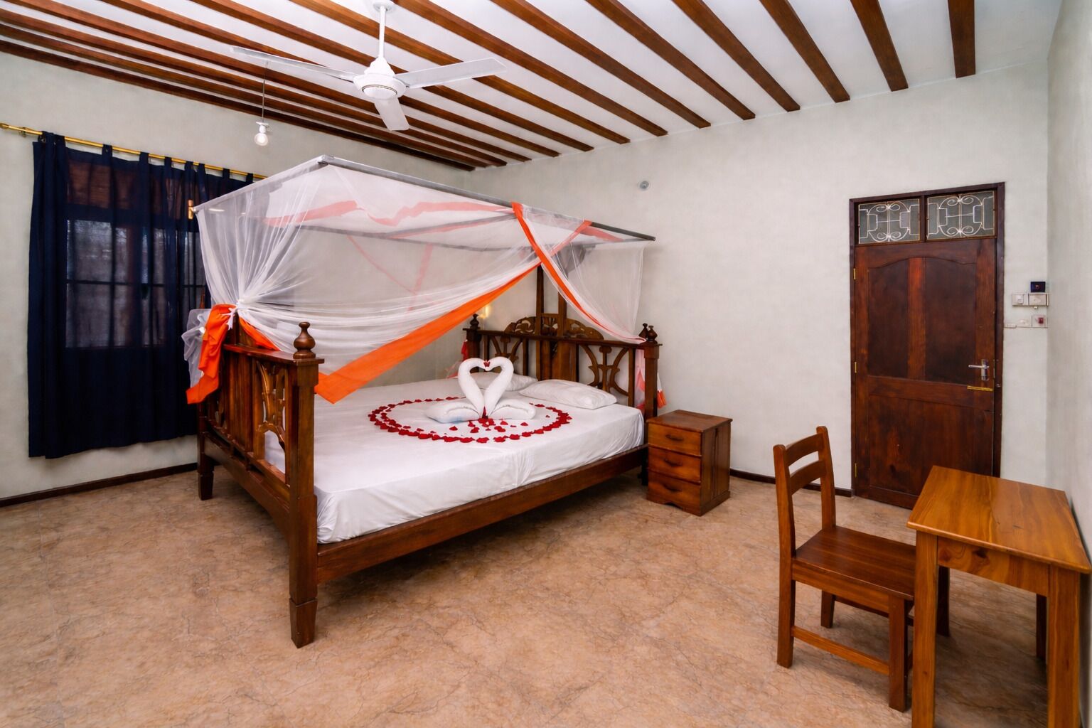 A wooden four-poster bed with a canopy, a small wooden nightstand, a wooden chair, and a wooden table.