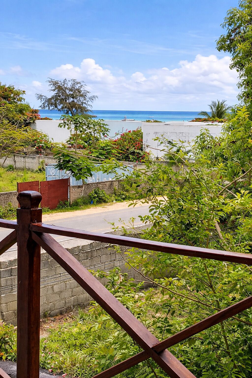A coastal view with a wooden railing, greenery, and a clear sky.