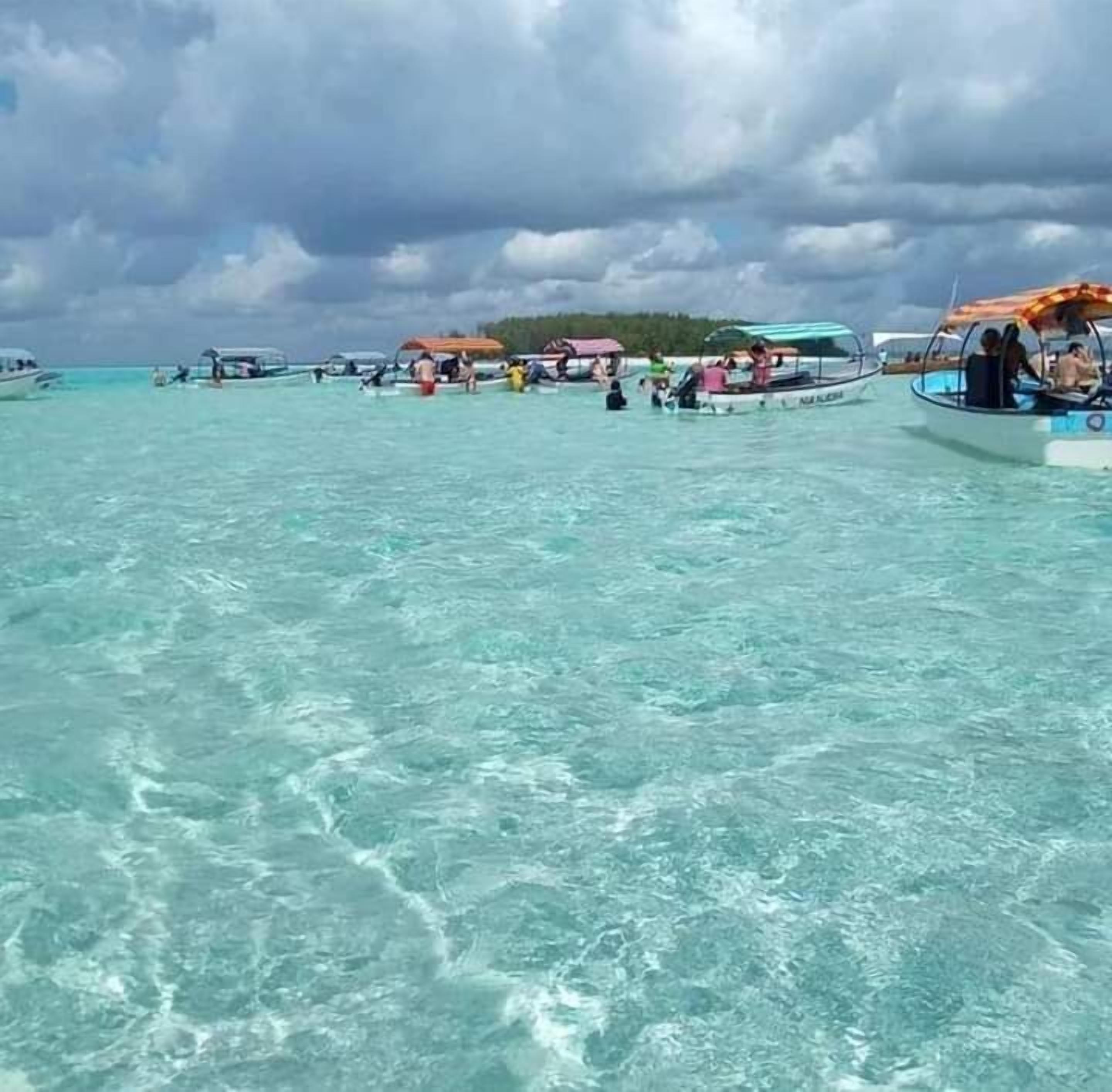 Une mer turquoise aux eaux limpides, avec des bateaux et des gens.