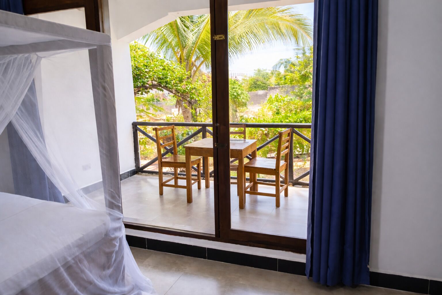 A balcony with a table and chairs, a bed with a canopy, and a view of greenery.