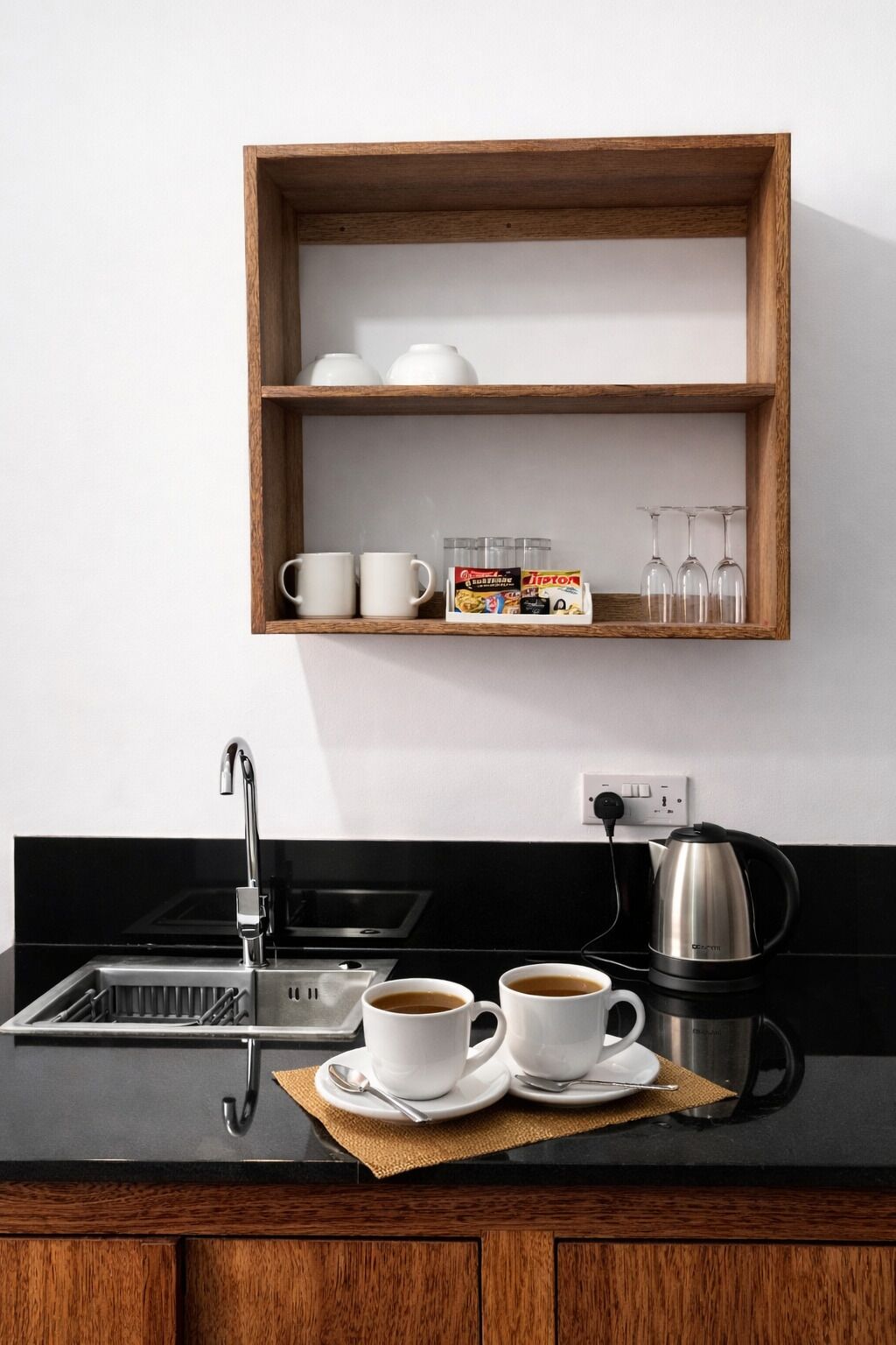 Una cucina con uno scaffale di legno che contiene tazze bianche, una macchina per il caffè e una scatola di tè Lipton.
