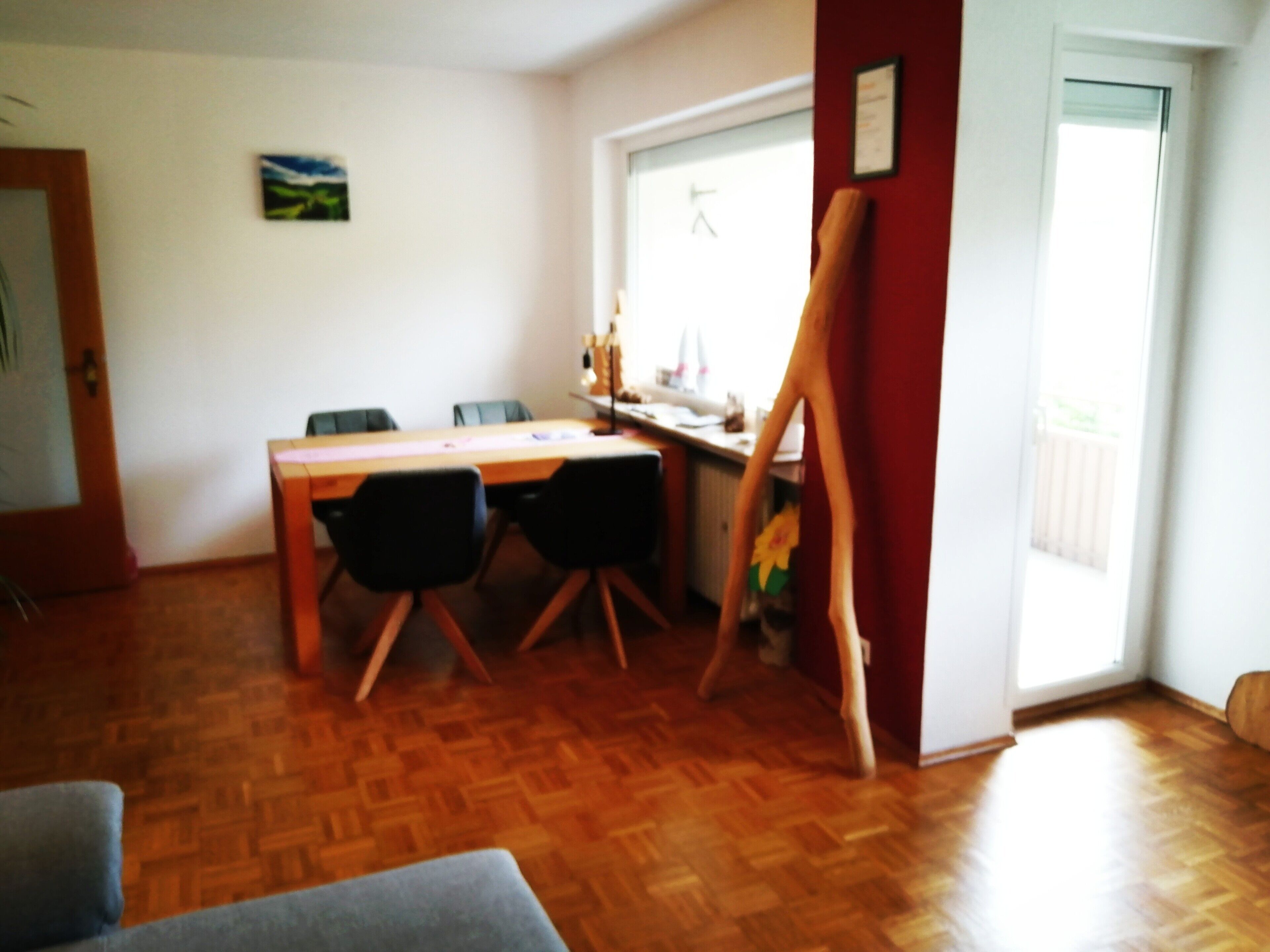 A room with a wooden floor, a dining table with chairs, a painting on the wall, and a window with a view.