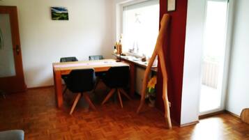 A room with a wooden floor, a dining table with chairs, a painting on the wall, and a window with a view.