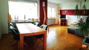 A dining area with a wooden table and chairs, a radiator, a television, and a sofa in a room with wooden flooring and a red accent wall. - Apartment 'Villingen' with Balcony and Wi-Fi (Villingen-Schwenningen)