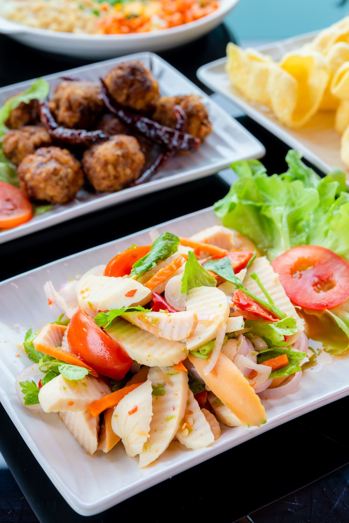 A variety of dishes including a salad with chicken, vegetables, and a side of meatballs.