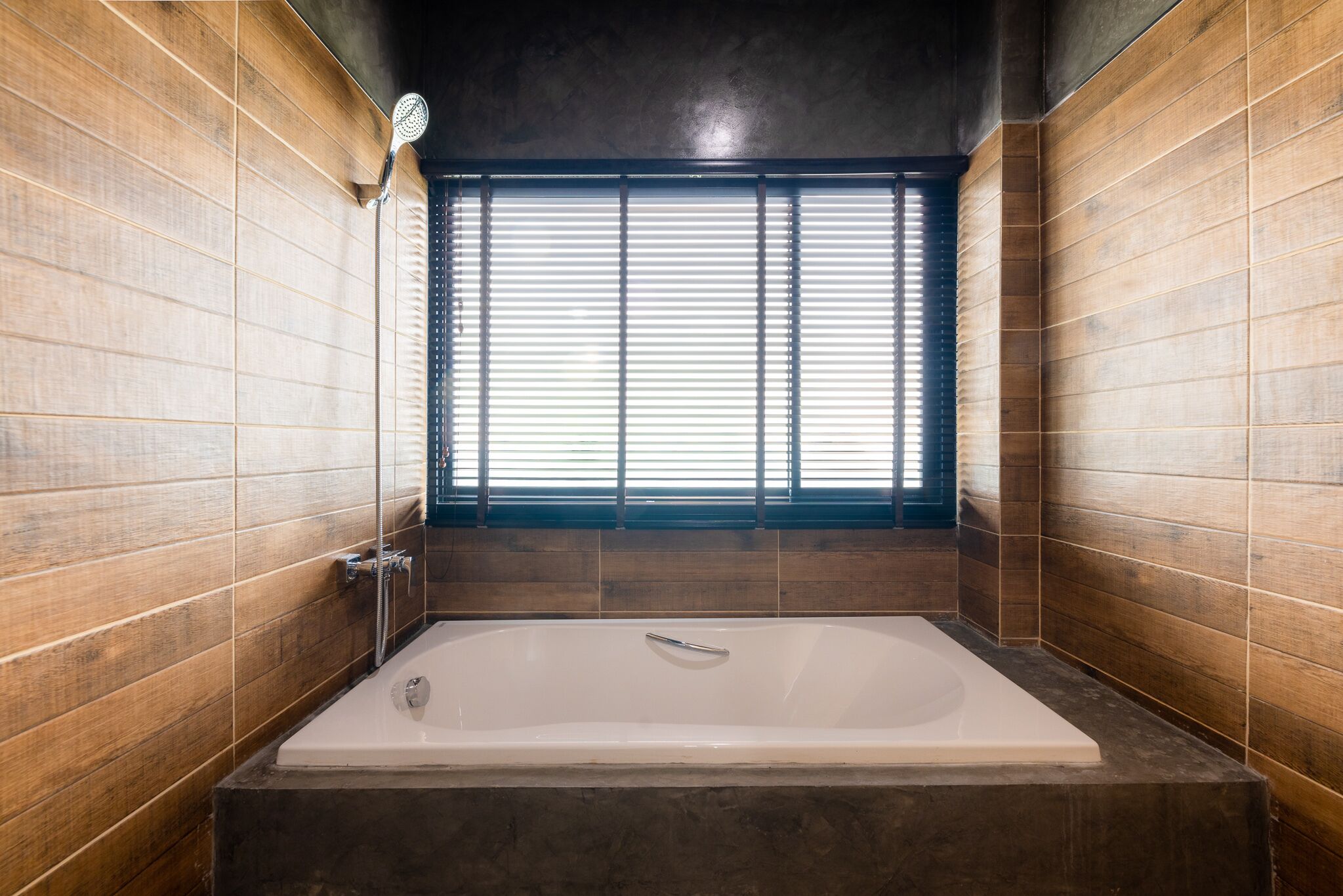 A modern bathroom with a large bathtub, wooden walls, and a window with blinds.