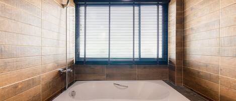 A modern bathroom with a large bathtub, wooden walls, and a window with blinds.
