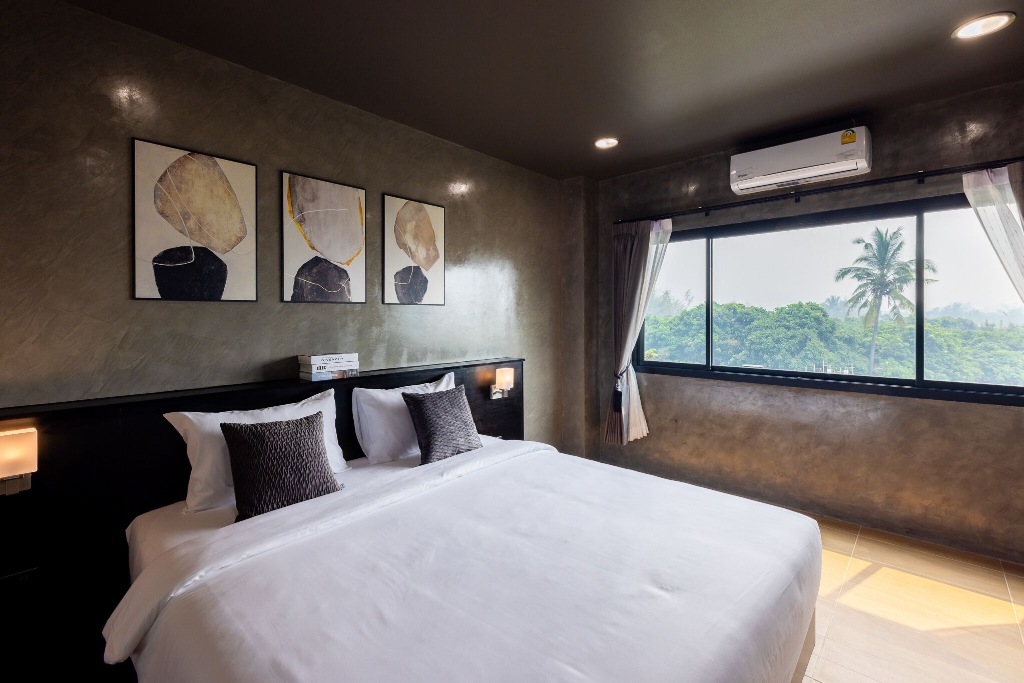 A hotel room with a large bed, a headboard with a light fixture, and a window with a view of palm trees.