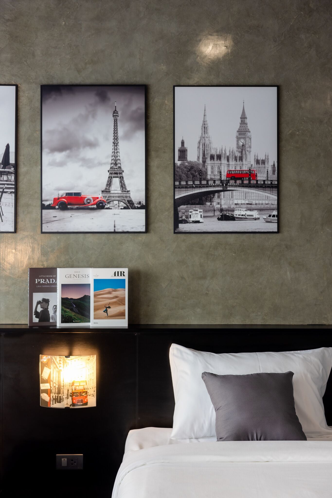A hotel room with a bed, pillows, and a wall with framed pictures of famous landmarks.