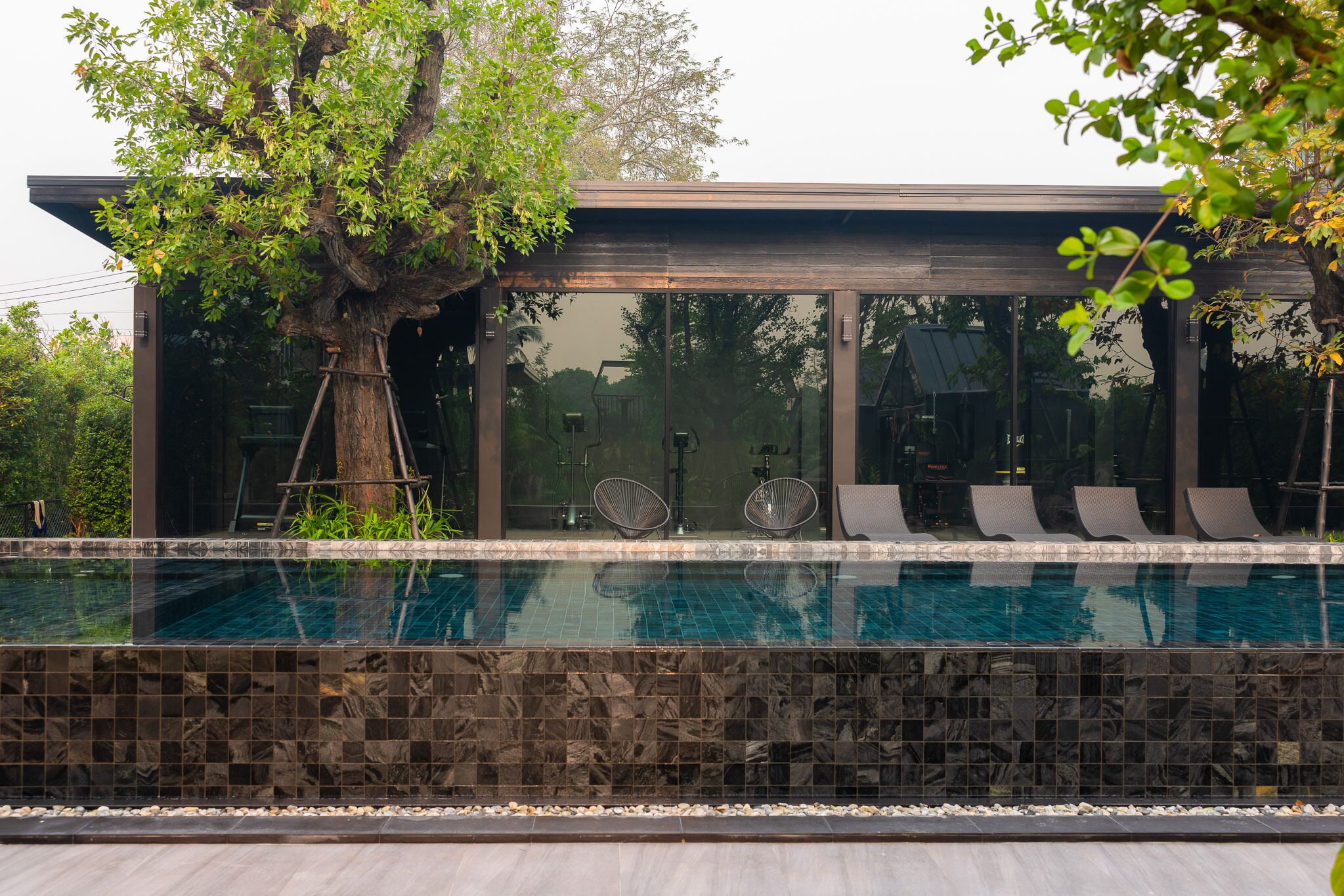 En moderne bygning med en glasfacade, en swimmingpool med flisekant og liggestole langs bassinkanten.