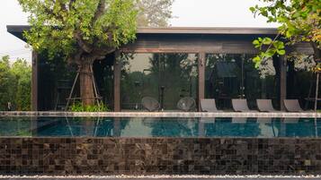 En moderne bygning med en glasfacade, en swimmingpool med flisekant og liggestole langs bassinkanten.