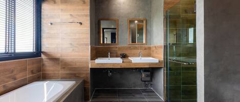 A modern bathroom with a bathtub, two sinks, a glass shower enclosure, and wooden accents.