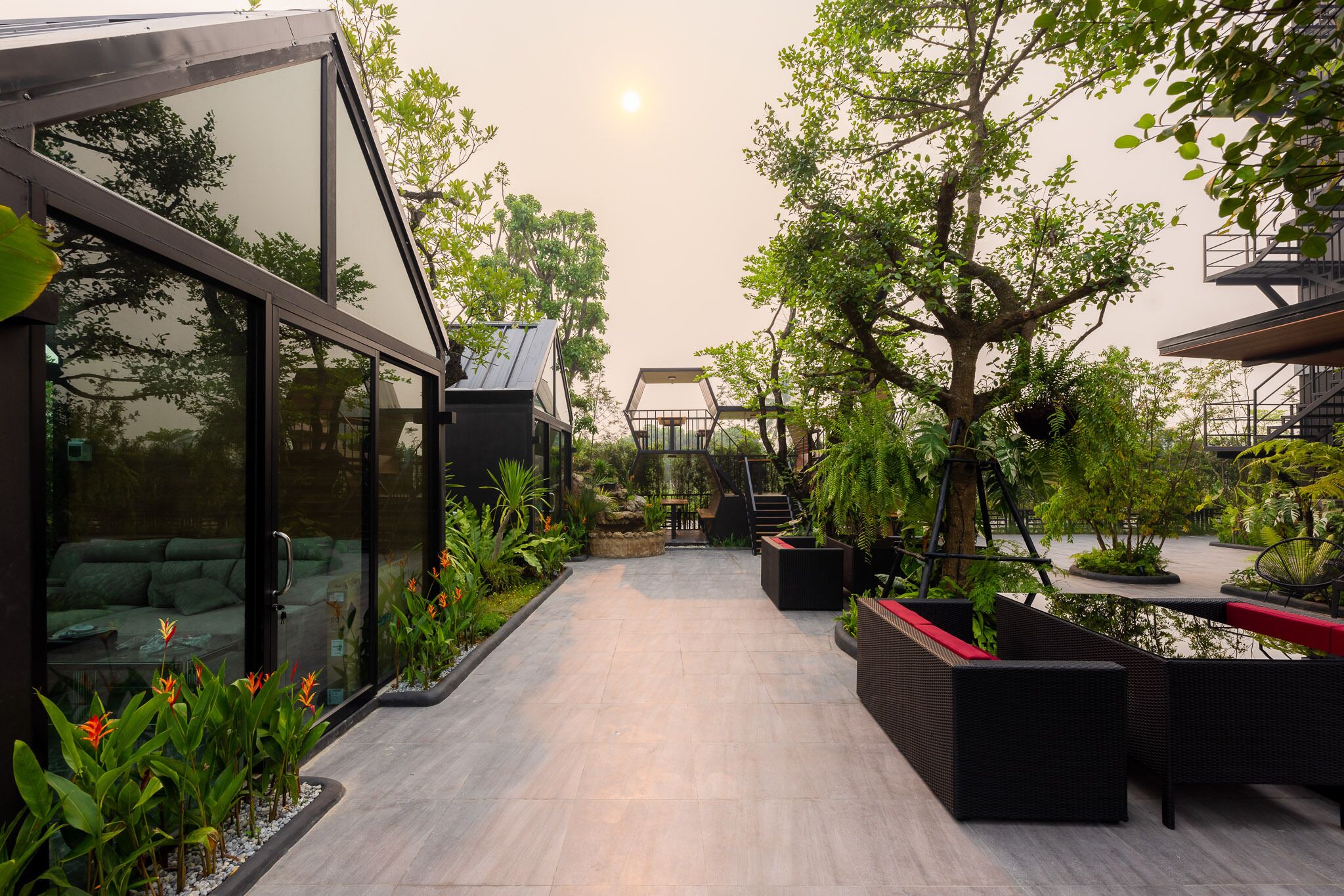A modern outdoor patio area with glass walls, outdoor seating, and lush greenery.