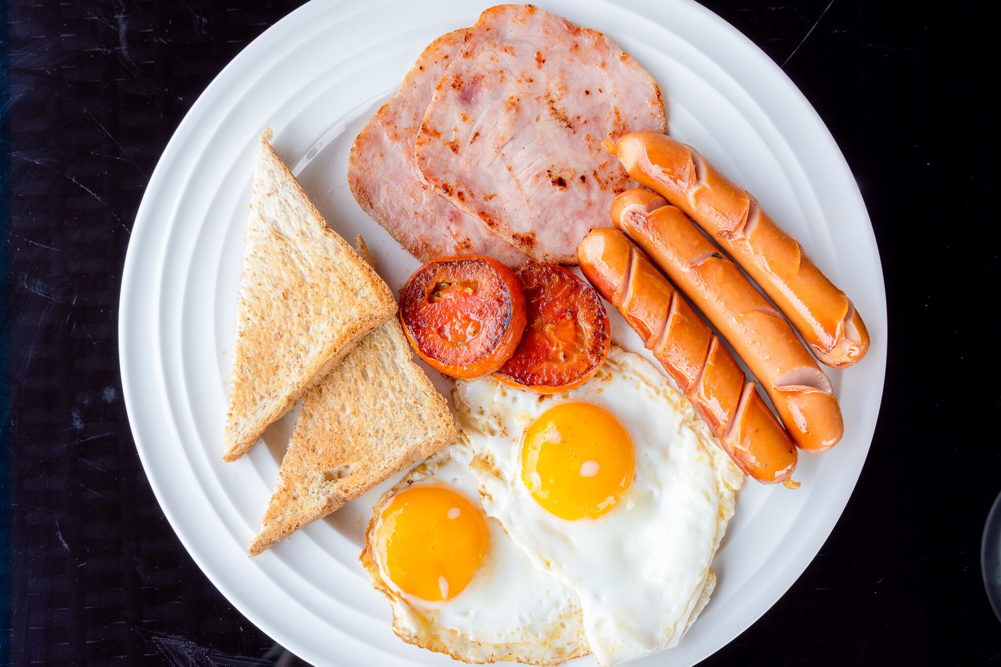 A plate with toast, eggs, sausages, and a slice of ham.