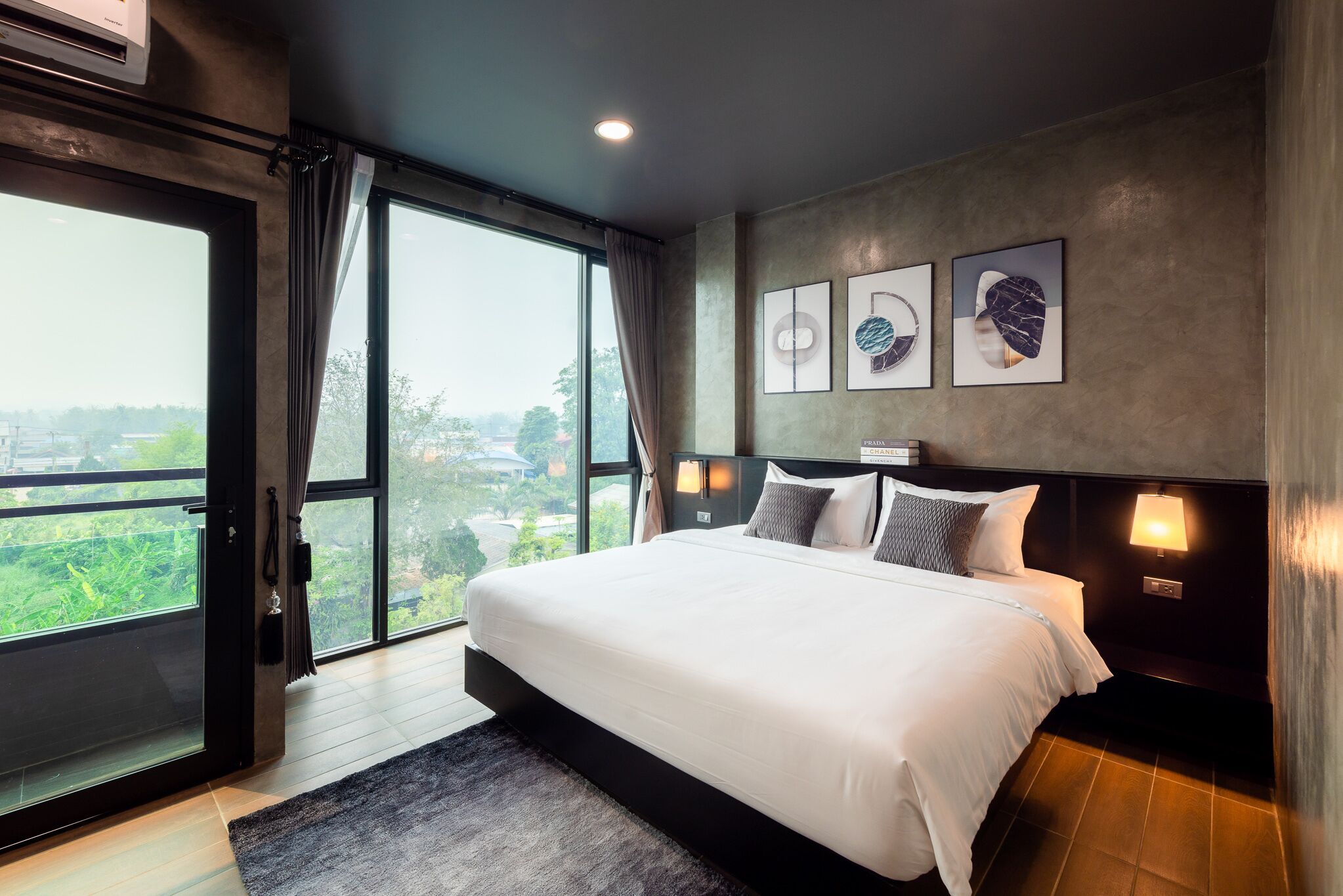 A modern bedroom with a large bed, a view through the window, and artwork on the wall.