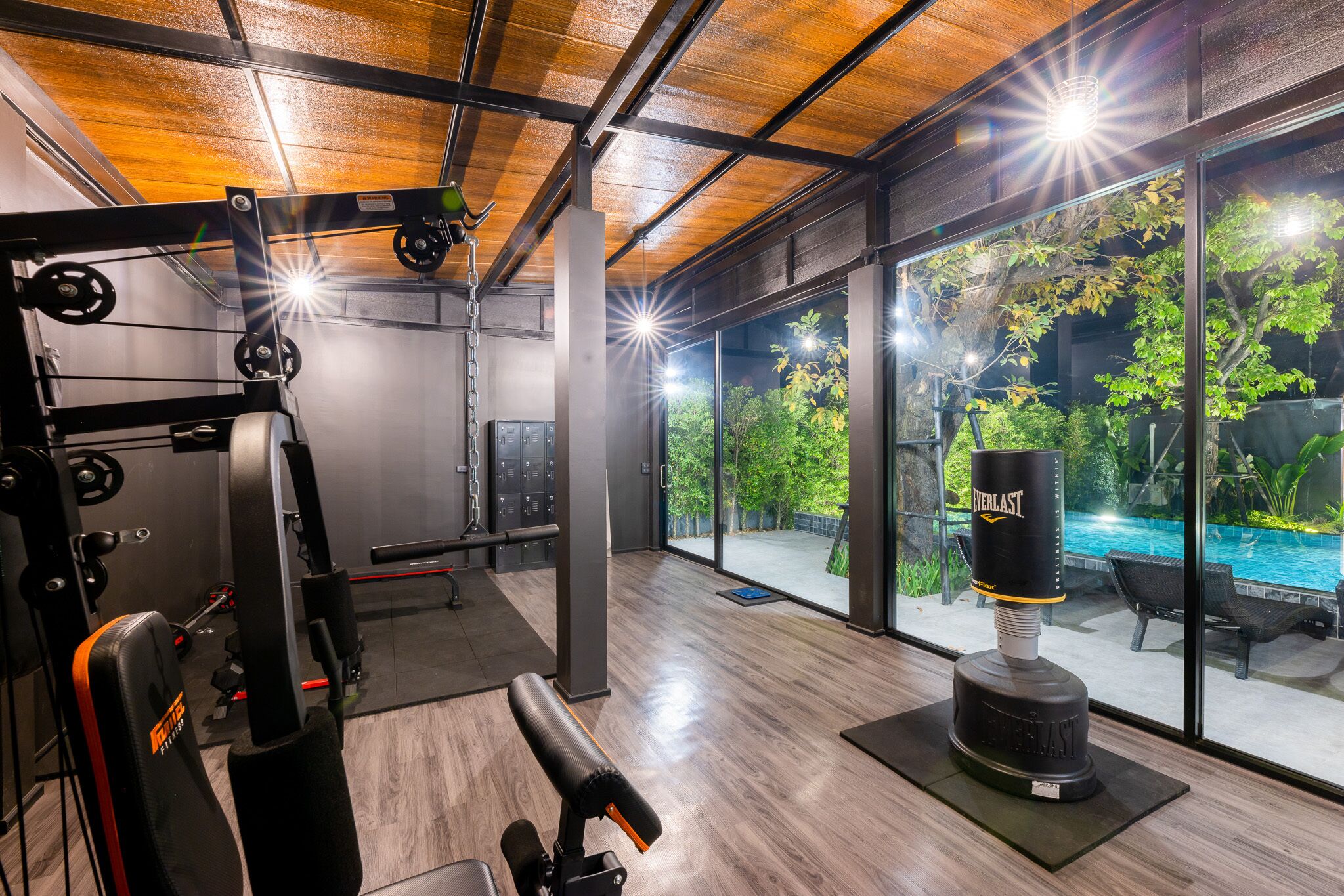 A gym with weightlifting equipment, a punching bag, and large windows overlooking a swimming pool.