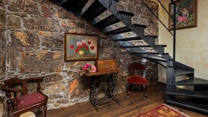 A room with a stone wall, a wooden chest of drawers, a vintage sewing machine, a red chair, and a black spiral staircase. - Rustic Villa Okra With Pool, Opatija - Ičići, Croatia (Opatija - Ičići)