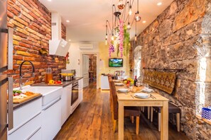 A modern kitchen with a brick wall, wooden flooring, and a dining area with a table set for two. - Rustic Villa Okra With Pool, Opatija - Ičići, Croatia (Opatija - Ičići)
