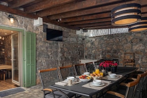 A dining area with stone walls, wooden beams, and a table set for breakfast with fruit and beverages.