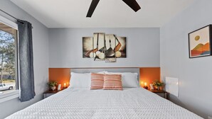 Ein ordentlich gemachtes Bett mit weißer Decke, zwei gestreifte Kissen und einem Kunstwerk darüber.