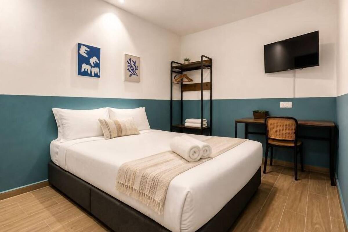 A hotel room with a bed, a desk, a chair, a TV, and artwork on the wall.