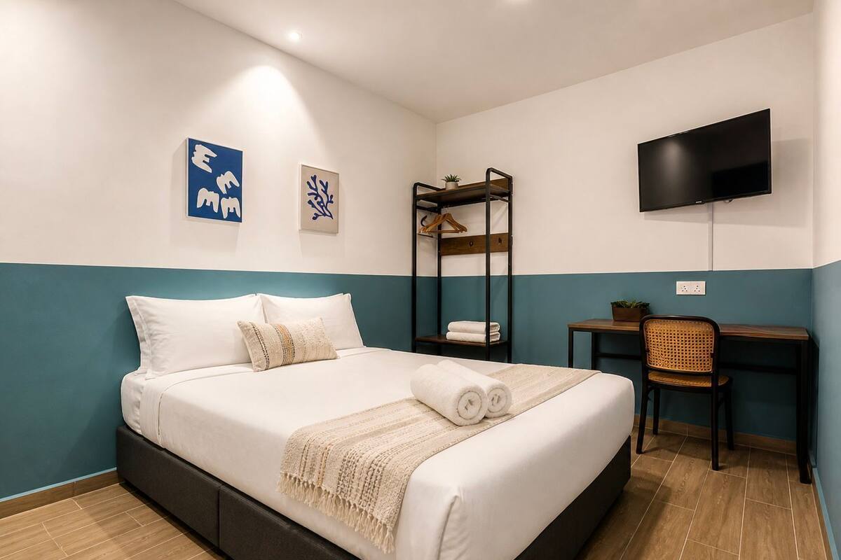 A hotel room with a bed, a desk, a chair, a TV, and artwork on the walls.