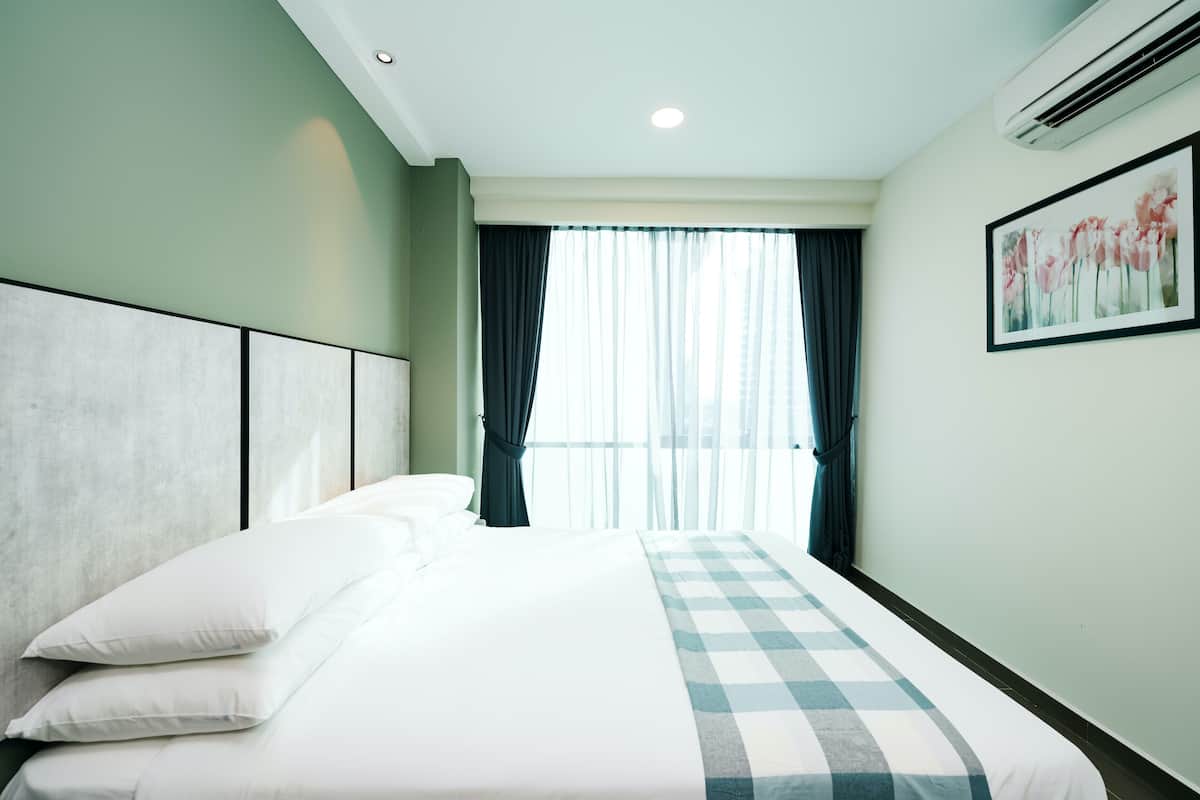 A hotel room with a large bed, a headboard, a window with curtains, an air conditioning unit, and a framed picture on the wall.
