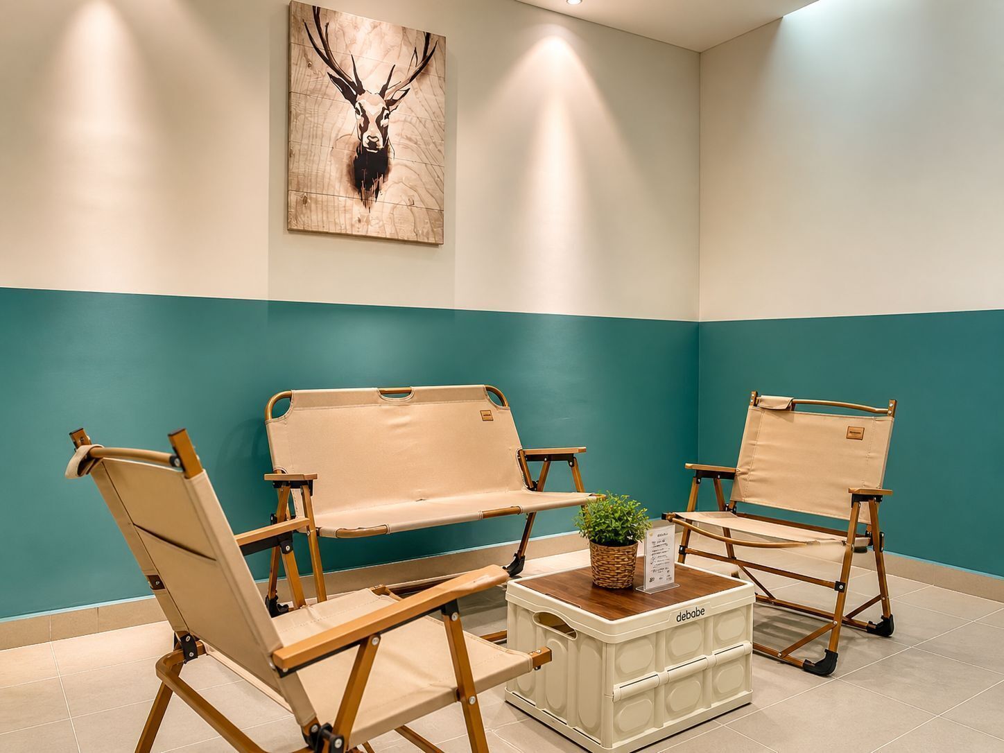 A room with teal and white walls, a wooden deer head artwork, and three beige canvas chairs with a small table and a plant.