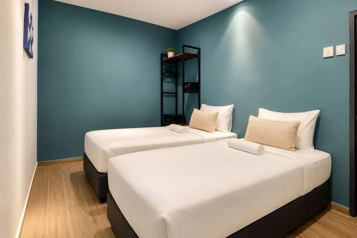 A room with two beds, a shelf with a plant, and a blue wall.
