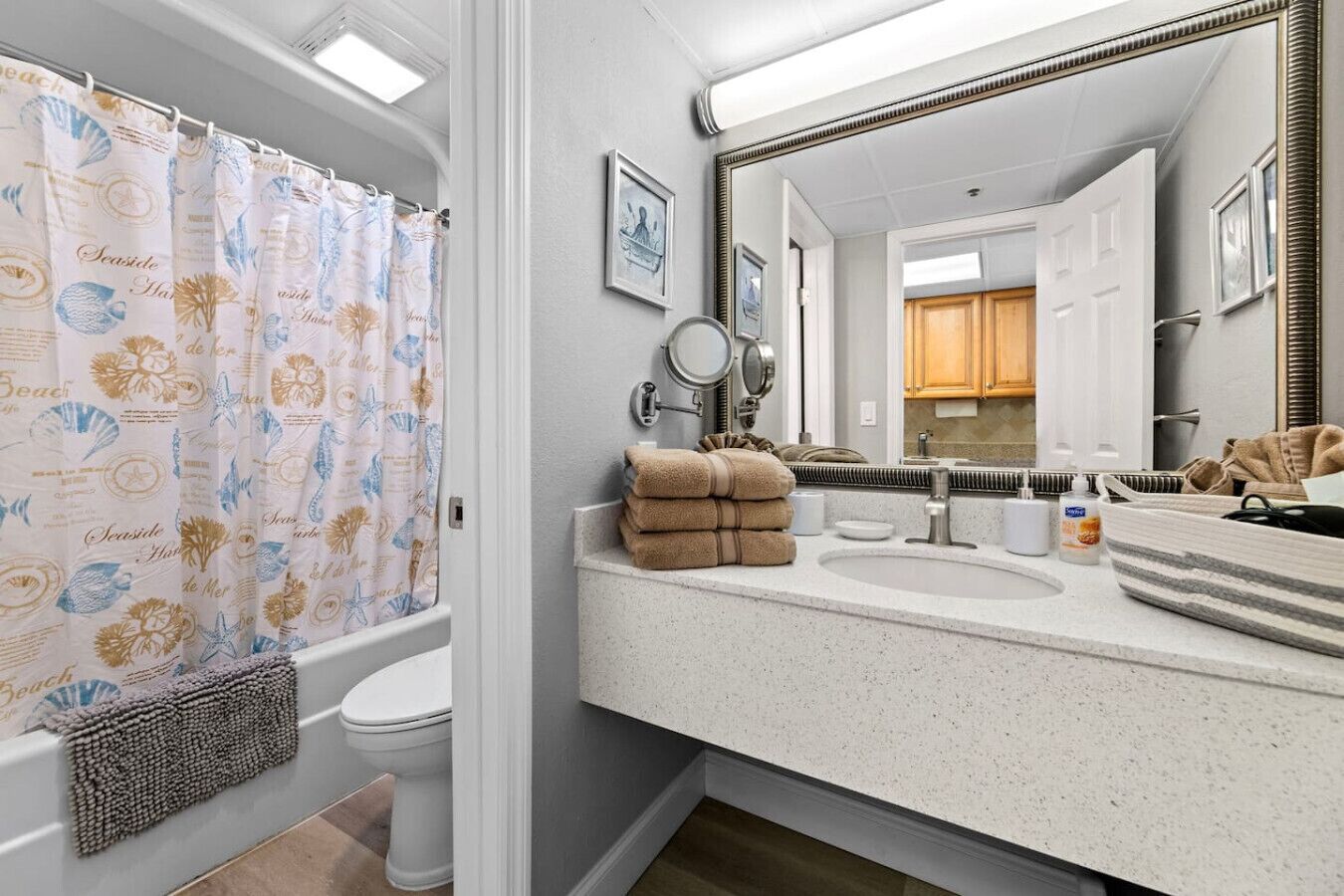 Ein Badezimmer mit Duschvorhang mit Strandmotiv, Toilette, Waschbecken mit Spiegel und Handtuchhalter.