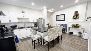 A modern kitchen with white cabinets, a black countertop, and a dining area with patterned chairs. - Cottage W LAKE VIEWS, beside waterfront trail and steps from beach (Barrie)