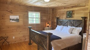 A wooden cabin bedroom with a bed, bedside table, lamp, and a window. - Good Hope Cottage- Amish Country / fire pit (Lawrenceburg)