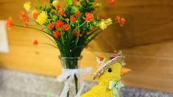 A decorative setup with a yellow chick figure, a vase of flowers, and carrots on a wooden board.