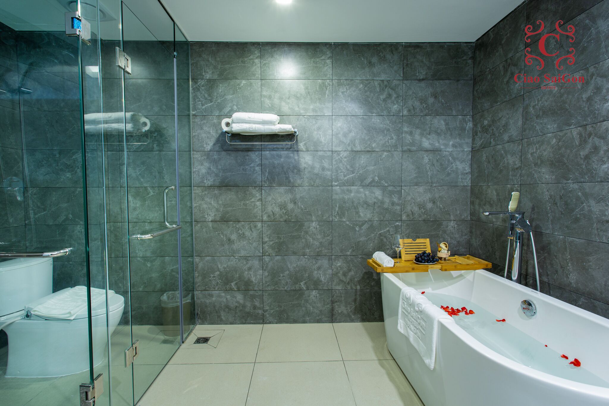 A modern bathroom with a glass-enclosed shower, a white bathtub with rose petals, and a towel rack with towels.