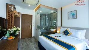 A hotel room with a bed, a shower area, a wooden partition, a vase with flowers, and a framed picture on the wall. - Ciao SaiGon 2 Hotel (Ho Chi Minh City)