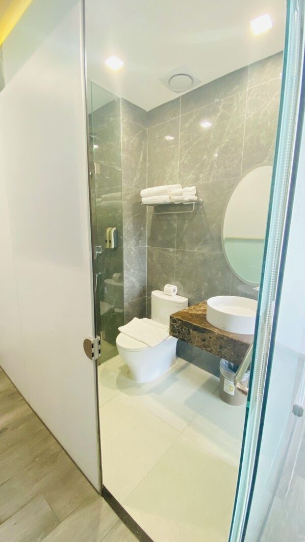 Un baño moderno con cabina de ducha de vidrio, inodoro, lavamanos y espejo.