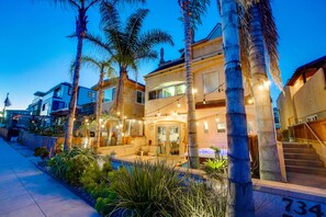A multi-story building with a balcony and outdoor seating area, surrounded by palm trees and plants. - Sanctuary@Mission Beach  (San Diego)