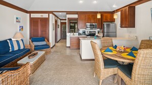 A modern kitchen with wooden cabinets, a central island, and a dining area with wicker furniture. - Updated ocean view retreat near Poipu Beach; A/C, pool, gym and restaurants. (Koloa)