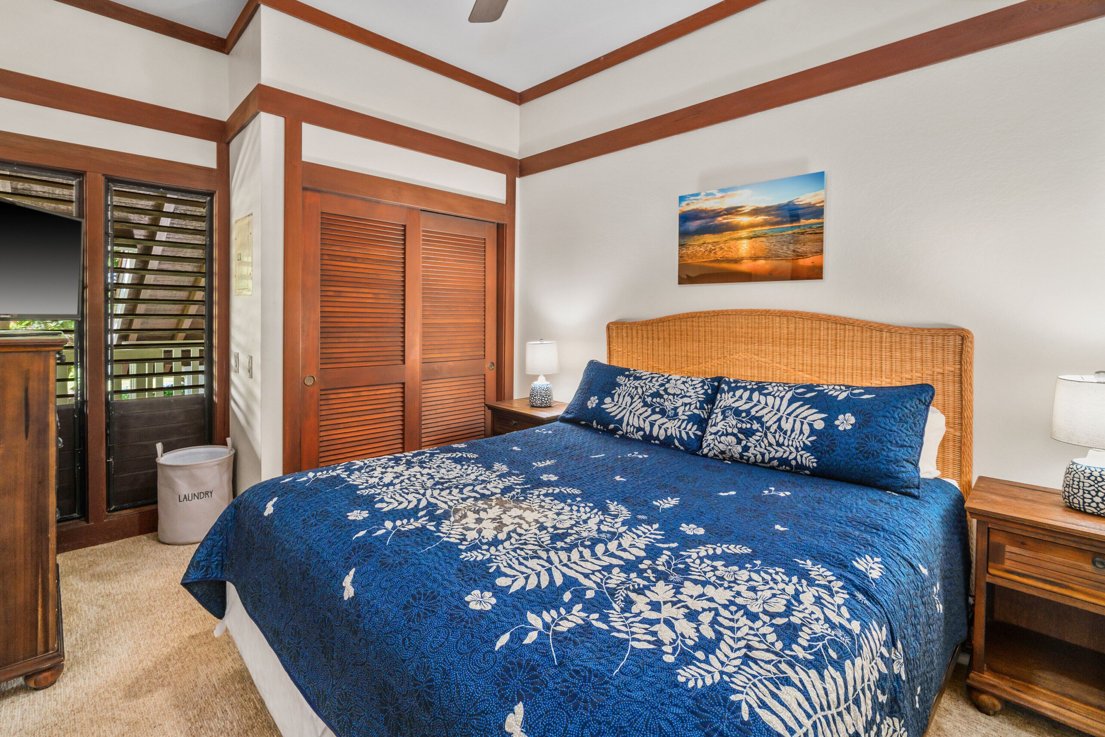 Une chambre avec un grand lit, une tête de lit en bois, une table de chevet, une lampe fixée au mur et une porte donnant sur l’extérieur.