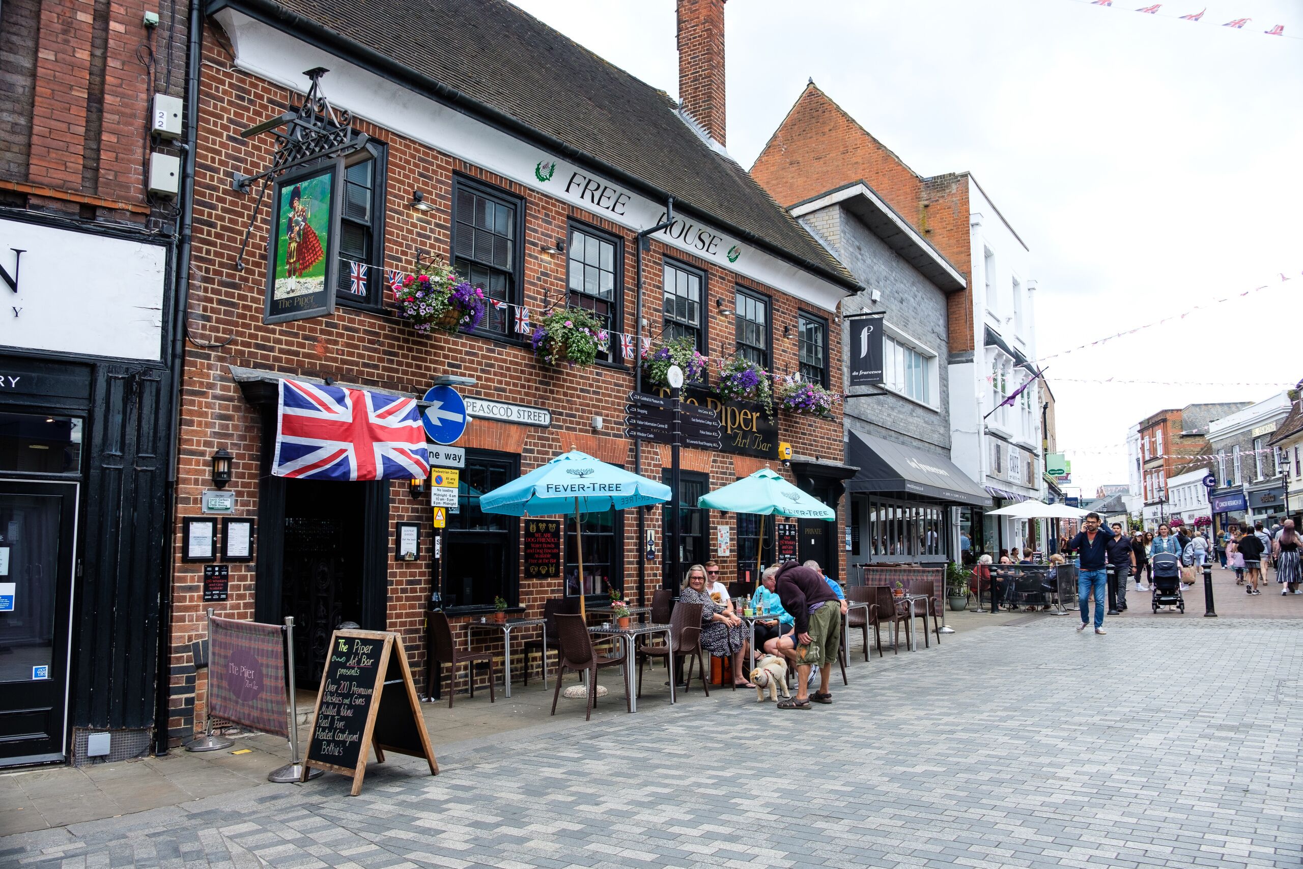Un pub doté d’une terrasse, arborant un drapeau britannique et affichant une enseigne indiquant « The Piper Art Bar ».