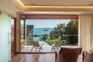 A balcony with a view of a pool and the sea, furnished with two chairs and a table.