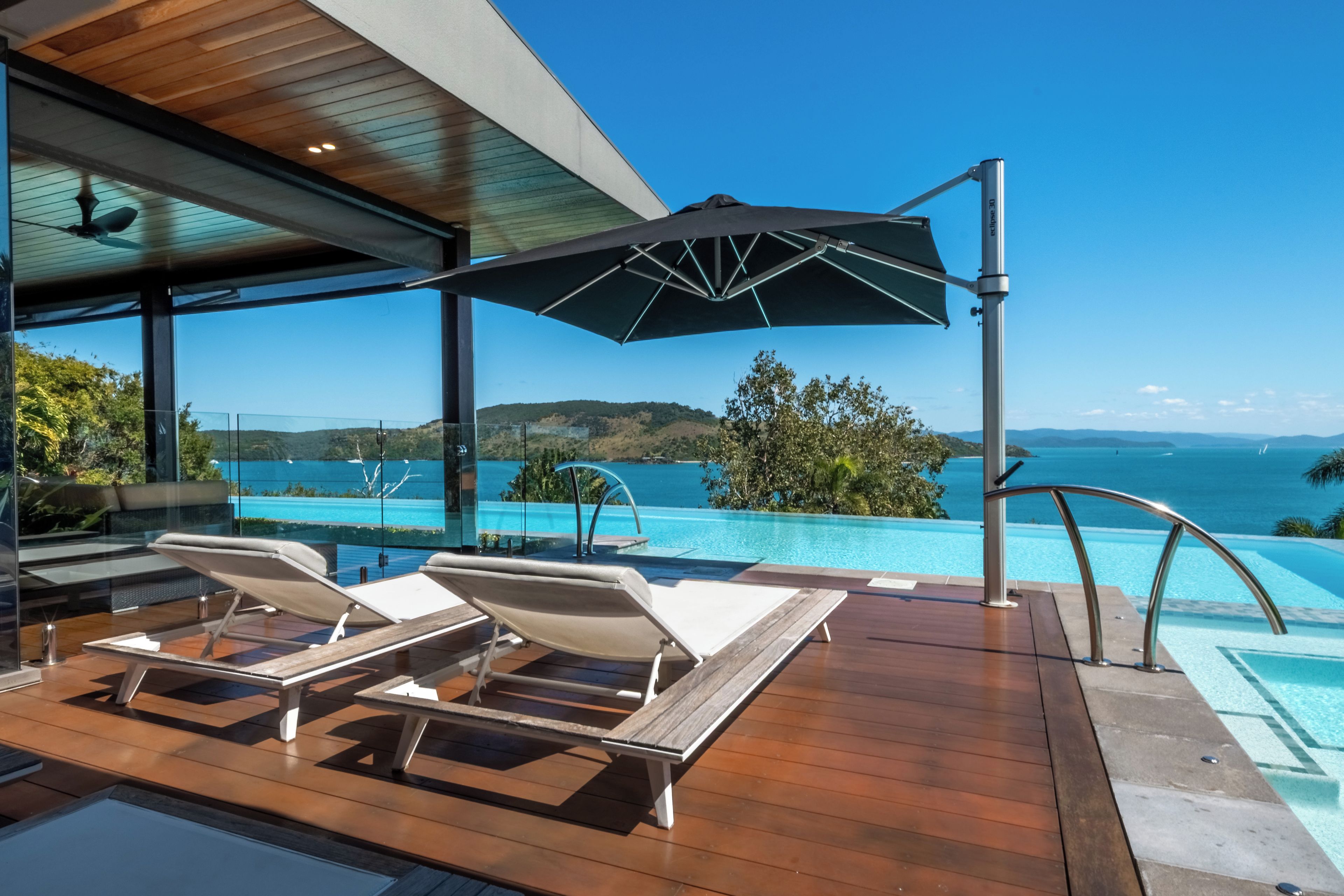 A modern outdoor pool area with lounge chairs and a view of the sea.