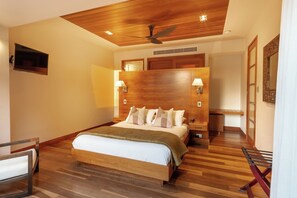 A hotel room with a wooden ceiling, a bed with multiple pillows, a nightstand, a TV, and a wooden floor.