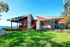 A modern house with a stone facade, large windows, and a covered patio overlooking a grassy yard.