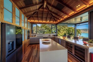 A modern kitchen with a large island, wooden cabinetry, and a view of the outdoors.